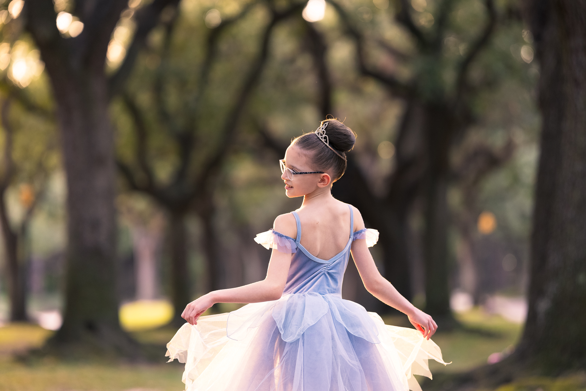 young ballet student twirls in blue tutu at sunset under canopy of live oaks